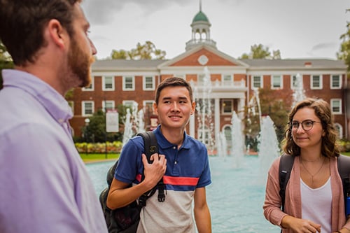 3 people standing in front of fountain and school building