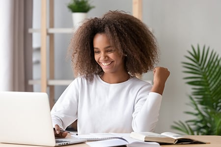 Estudiante mirando la computadora portátil sonriendo y levantando un puño triunfante